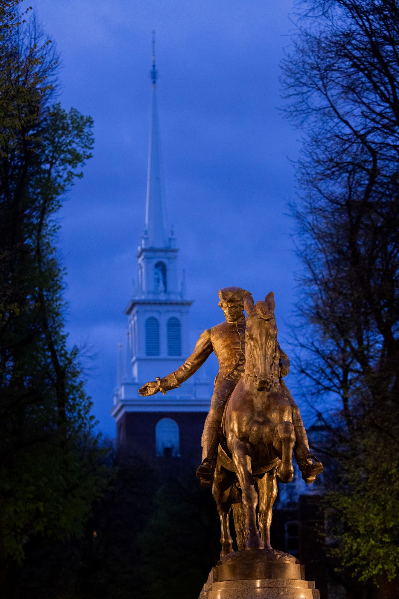 A statue of Paul Revere riding a horse in front of Old North Church in Boston at magic hour.